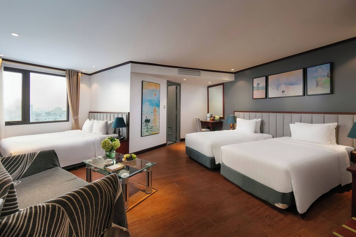 A hotel room with two beds, a sofa, a glass coffee table, and artwork on the walls.