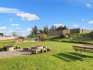 A playground with a slide and climbing structures, surrounded by a grassy area with benches and a picnic table. - 4 Star Holiday Home in Lokken (Lokken)