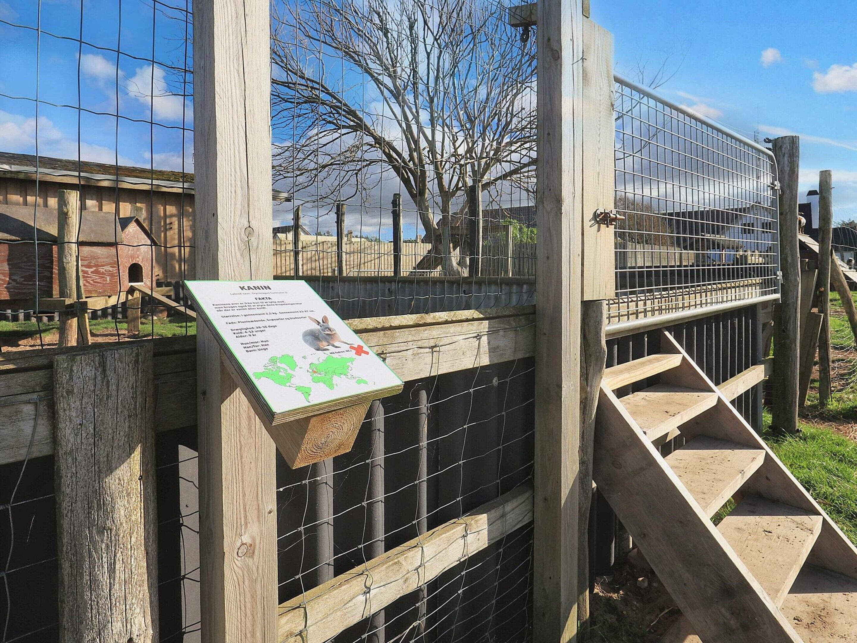 A wooden fence with a metal gate, a wooden staircase, and a sign with a map and text.