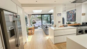 A modern kitchen with a built-in oven, a dining area with a wooden table, and a view of a garden through large windows.