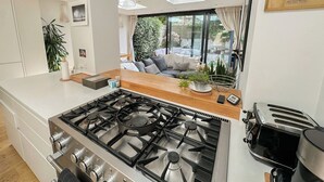 A modern kitchen with a gas stove, a toaster, and a large window overlooking a garden.