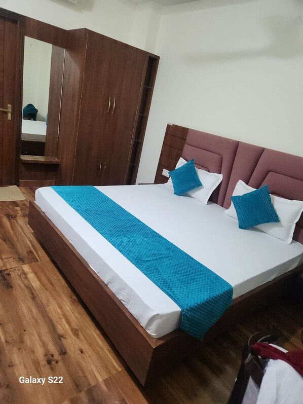 A bedroom with a large bed, wooden wardrobe, and a mirror. - Motel Dwarika (Roorkee)