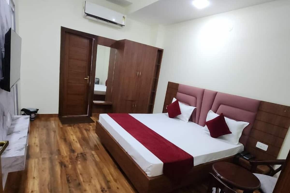 A bedroom with a wooden floor, a bed with a red and white bedspread, a ceiling fan, and a wardrobe.