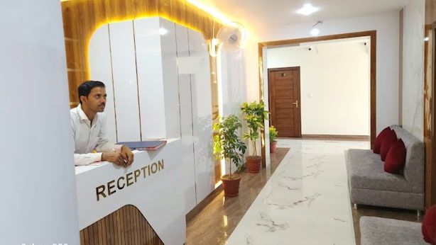 A reception area with a reception desk labeled "RECEPTION," a wooden reception desk, potted plants, a grey sofa with red cushions, and a marble floor.