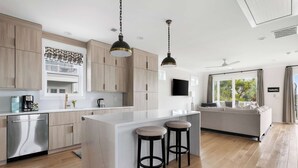 Een moderne keuken met houten kastjes, een centraal eiland met krukken, roestvrijstalen apparatuur en hangende lampen.
