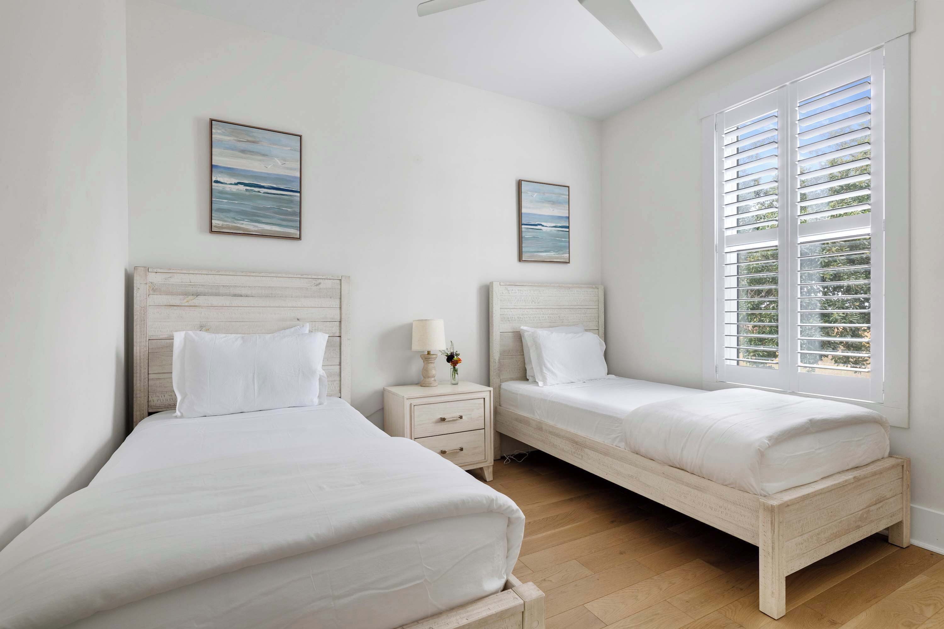 A bedroom with two single beds, a nightstand with a lamp, and a window with blinds.