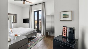A modern hotel room with a bed, a coffee maker, a TV, and a view of the city through large windows.