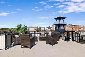 A rooftop terrace with wicker furniture, a small table, and a view of the cityscape.