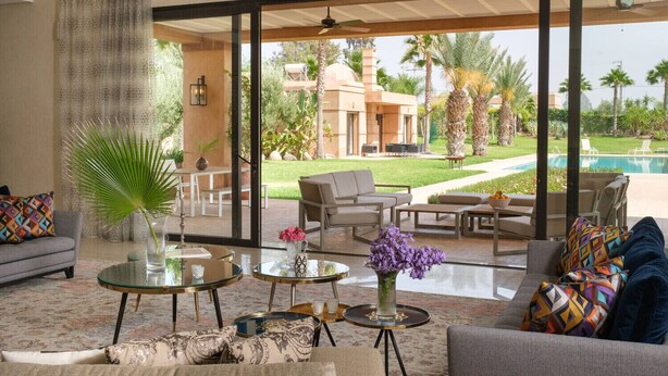 A spacious living area with a large glass door leading to a pool and outdoor seating. - TAMARI (Marrakech)