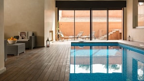 A pool area with wicker furniture, a bowl of fruit, and a view of a building through a glass door. - TAMARI (Marrakech)