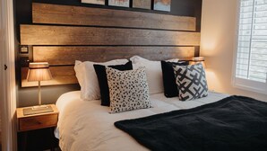 Ein ordentlich bezogenes Bett mit einer schwarzen Tagesdecke, einem Holzkopfteil und mehreren Kissen in verschiedenen Mustern.