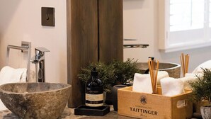 Ein modernes Badezimmer mit einem Steintonne, einer Holzkiste mit Pflegeprodukten und einem gerahmten Kunstwerk an der Wand.