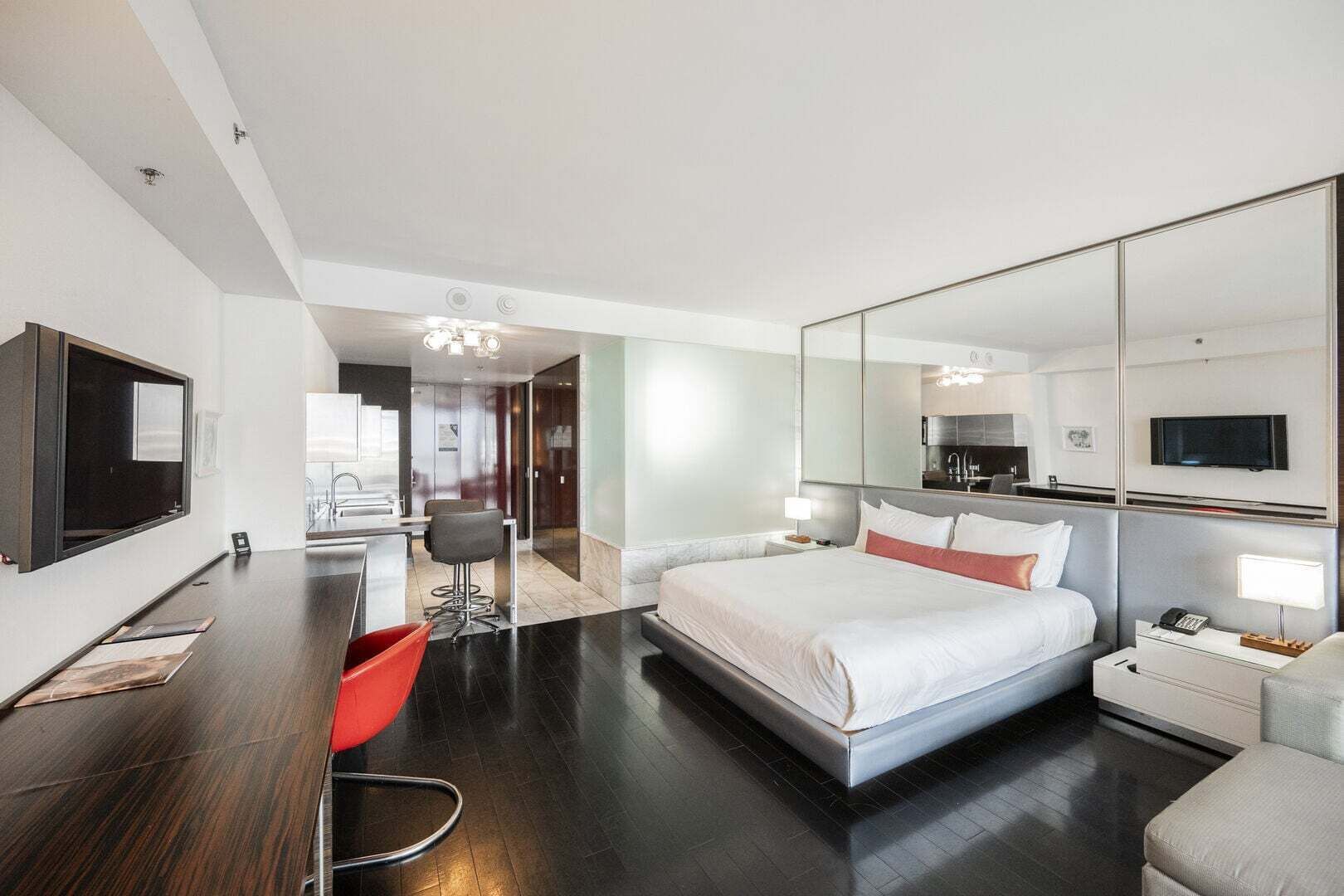 Una habitación de hotel moderna con una cama grande, un escritorio, una silla, un televisor y un espejo.