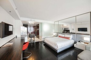 Quarto de hotel moderno com uma cama grande, uma escrivaninha, uma cadeira, uma televisão e um espelho.