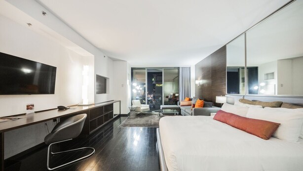 A modern hotel room with a large bed, a desk with a chair, a TV, and a large mirror. - SVS: Strip View Studio | Open Balcony | Full Size Fridge | Palms Place (Las Vegas)
