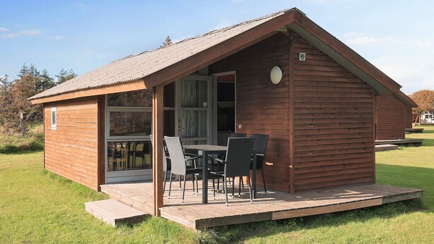 A wooden cabin with a patio area, a dining table, and chairs. - 5 Star Holiday Home in Lokken (Lokken)