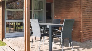 A wooden cabin with a covered patio area featuring a table and chairs. - 5 Star Holiday Home in Lokken (Lokken)