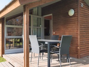 A wooden cabin with a covered patio area featuring a table and chairs. - 5 Star Holiday Home in Lokken (Lokken)