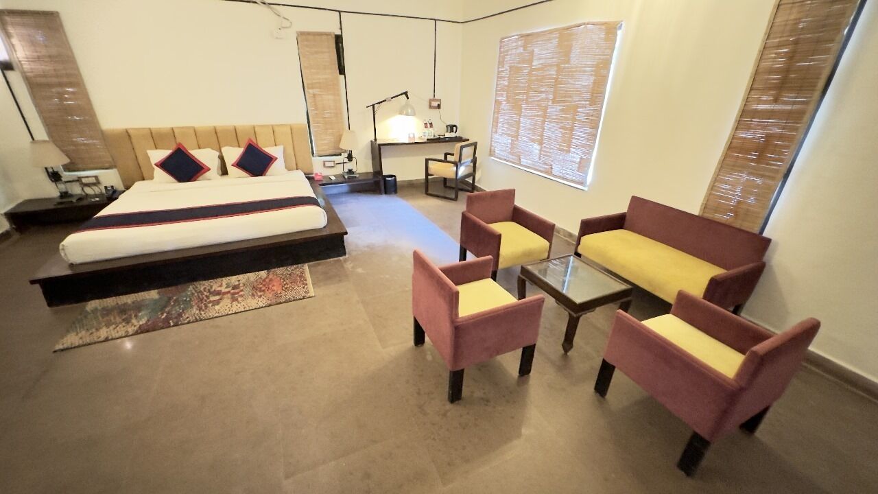 A modern hotel room with a large bed, a desk, two armchairs, and a sofa.