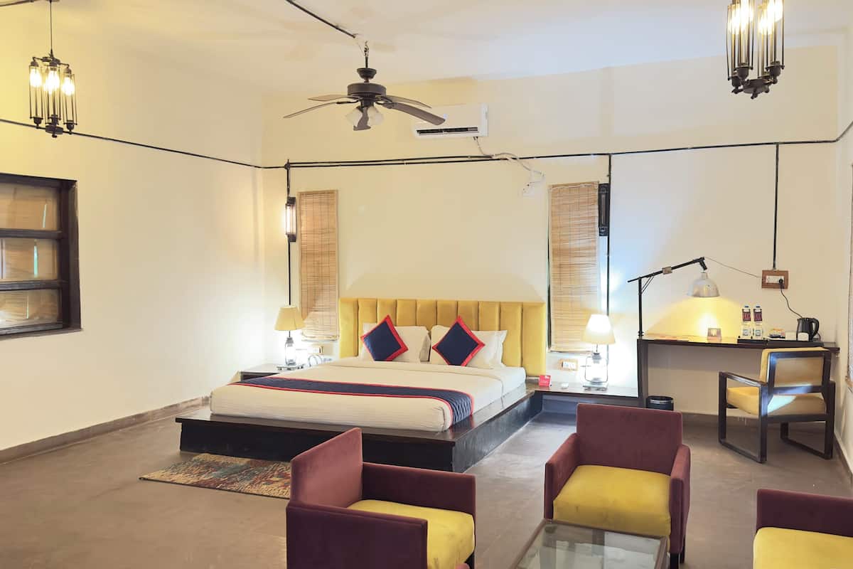 Ein Hotelzimmer mit einem Bett, zwei Stühlen, einem Schreibtisch, einem Deckenventilator und einem Fenster mit Jalousien.