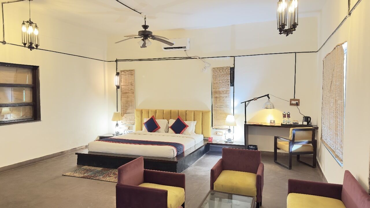 Habitación de hotel con cama, dos sillones, escritorio y ventilador de techo.