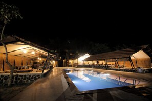 A swimming pool with a stone border, surrounded by covered seating areas and a stone wall. - Spree Maati Jungle Resort (Manpur)