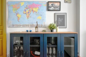 A world map, framed artwork, and a cabinet with wine glasses.