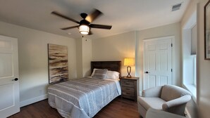 A bedroom with a bed, a chair, a nightstand, a ceiling fan, and a painting on the wall. - The Traveler on Main Suite #12- Across the Street from Back of the Dragon! (Tazewell)