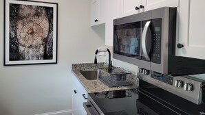 A modern kitchen with white cabinetry, a stainless steel refrigerator, a microwave, and an oven. - The Traveler on Main Suite #12- Across the Street from Back of the Dragon! (Tazewell)