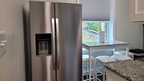 A stainless steel refrigerator with a water dispenser, a white table with chairs, and a window with blinds. - The Traveler on Main Suite #12- Across the Street from Back of the Dragon! (Tazewell)