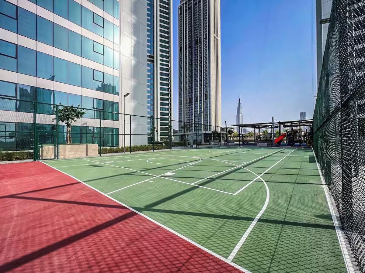 Un court de tennis en plein air, doté d’une surface rouge et verte, entouré de bâtiments modernes.