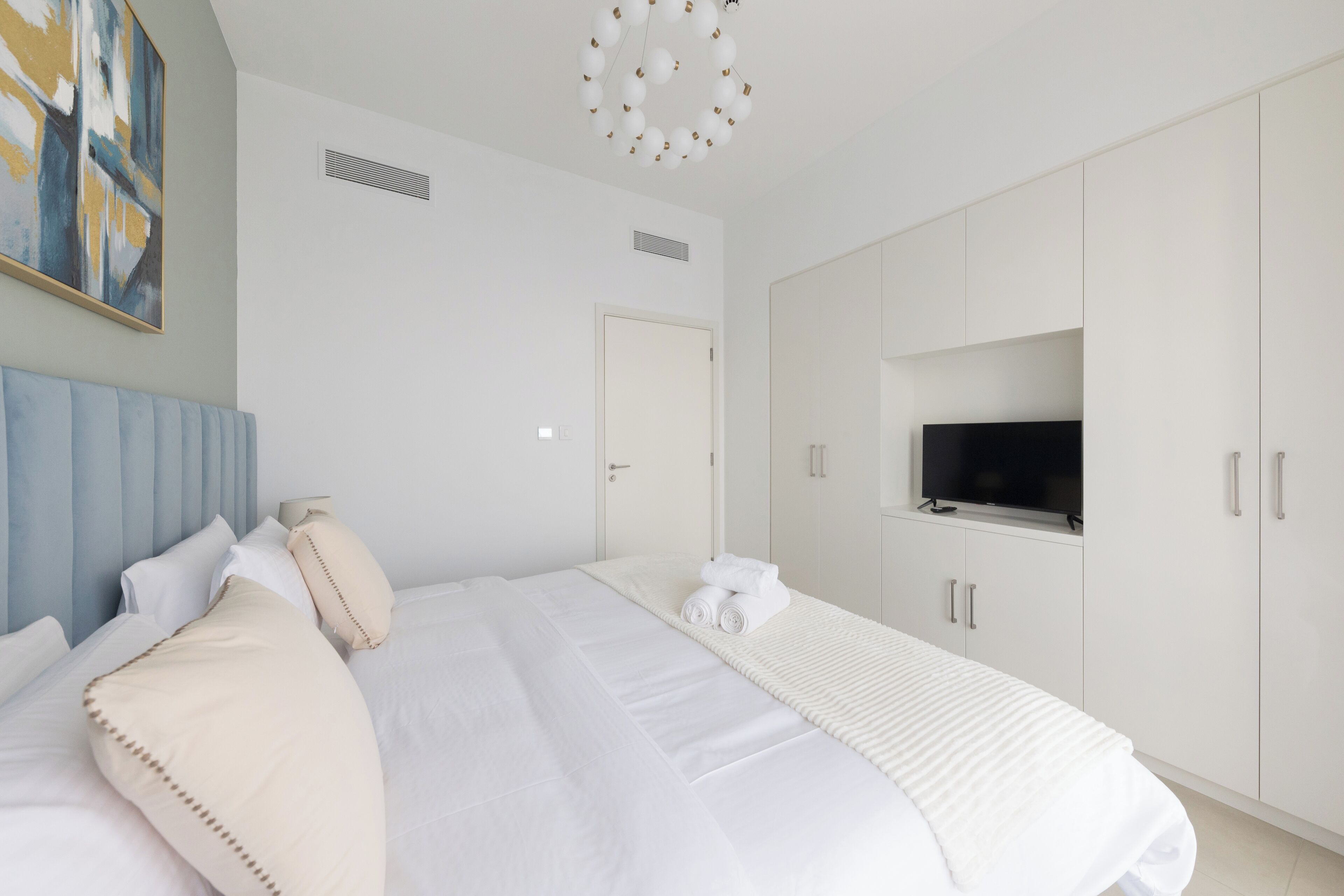 A modern bedroom with a large bed, a TV mounted on the wall, and a minimalist design.