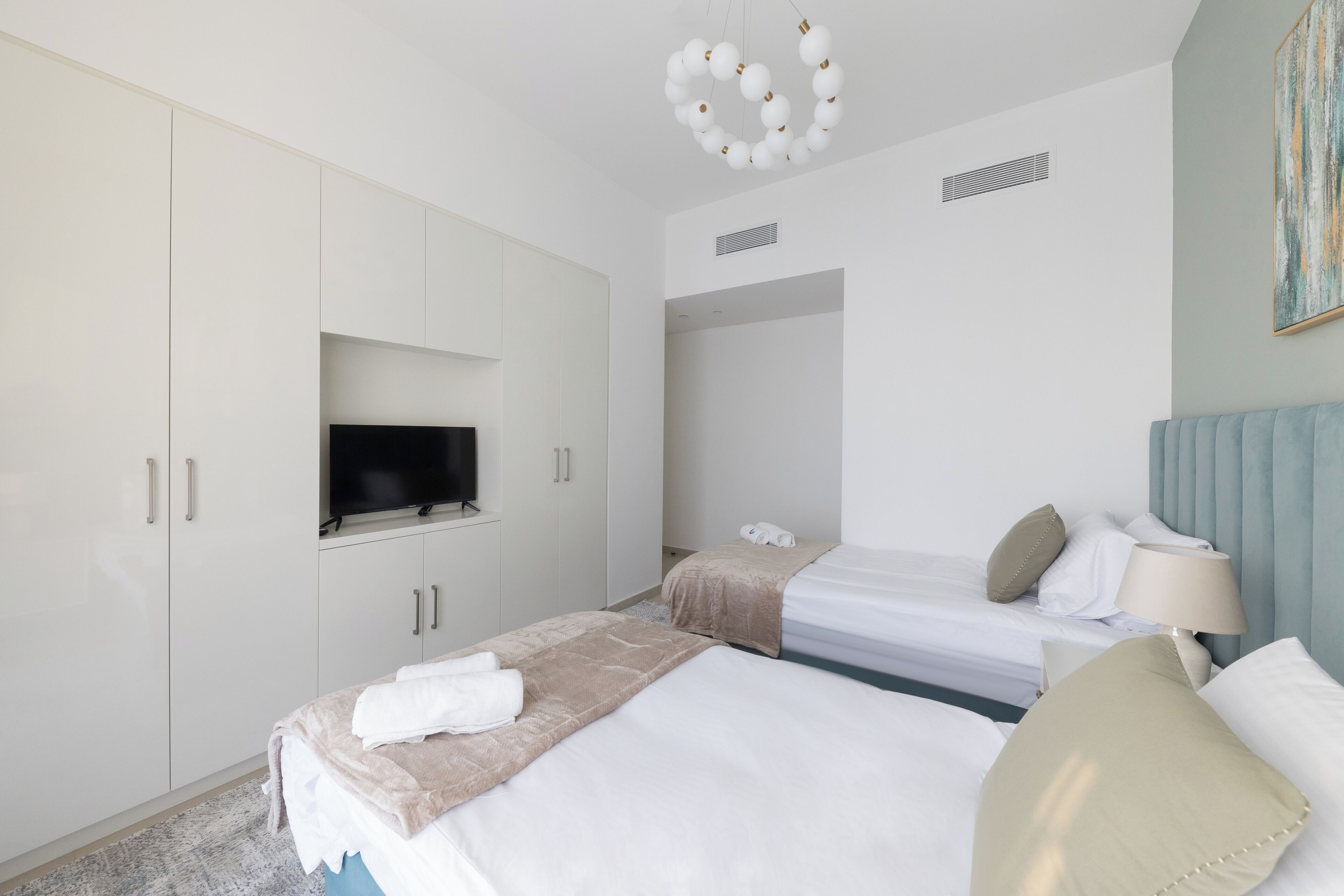 A hotel room with two beds, a TV mounted on a cabinet, a ceiling light fixture, and a painting on the wall.
