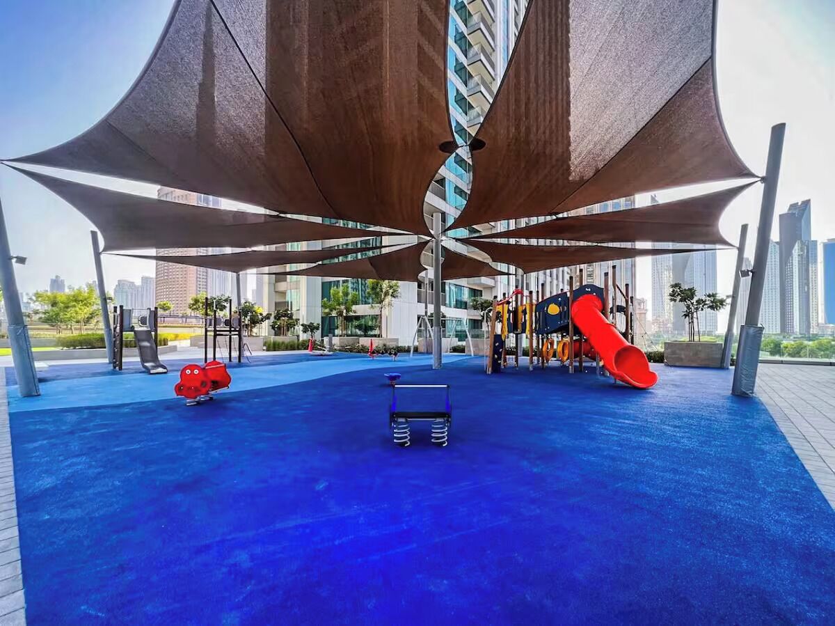 A playground with a blue rubber surface, a red slide, and a climbing structure.