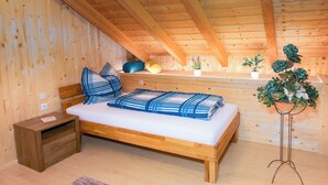 A wooden bedroom with a sloped ceiling, a bed with blue and white bedding, a nightstand, and two potted plants.