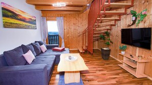 A wooden interior with a sofa, TV, staircase, and a painting on the wall.