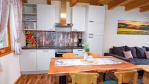A modern kitchen with white cabinets, a wooden dining table, and a painting of a sunset on the wall.