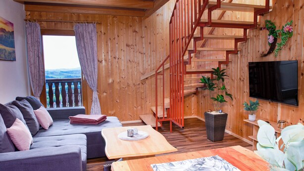 A wooden interior with a sofa, a coffee table, a TV, and a staircase.