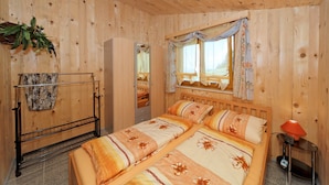 A wooden cabin room with a bed, a window with curtains, a plant, and a towel rack. - Villa Hügl - cozy vacation apartment for couples (Waldkirchen)