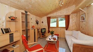 A cozy wooden cabin with a white sofa, a red chair, a TV, and a small table with a vase of flowers. - Villa Hügl - cozy vacation apartment for couples (Waldkirchen)