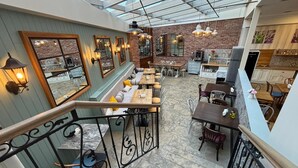 Ein Restaurant mit hoher Decke, freiliegenden Backsteinwänden und vielfältigen Sitzgelegenheiten, darunter Tische und Bänke.
