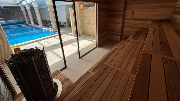 Ein Saunaraum mit Holzboden, einer Glastür zum Poolbereich und einer Sitzbank.