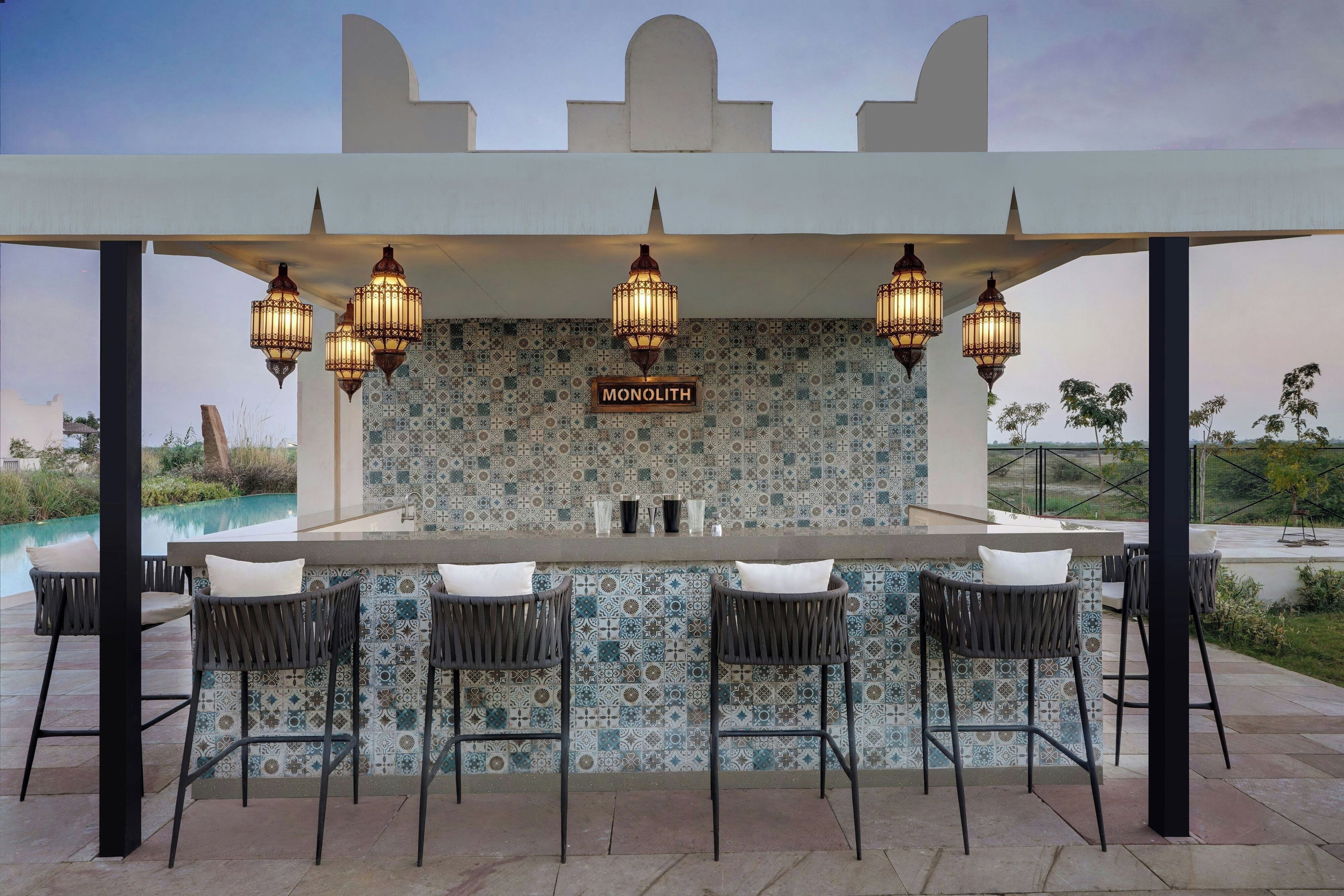 A bar area with a tiled backsplash, hanging lanterns, and bar stools.