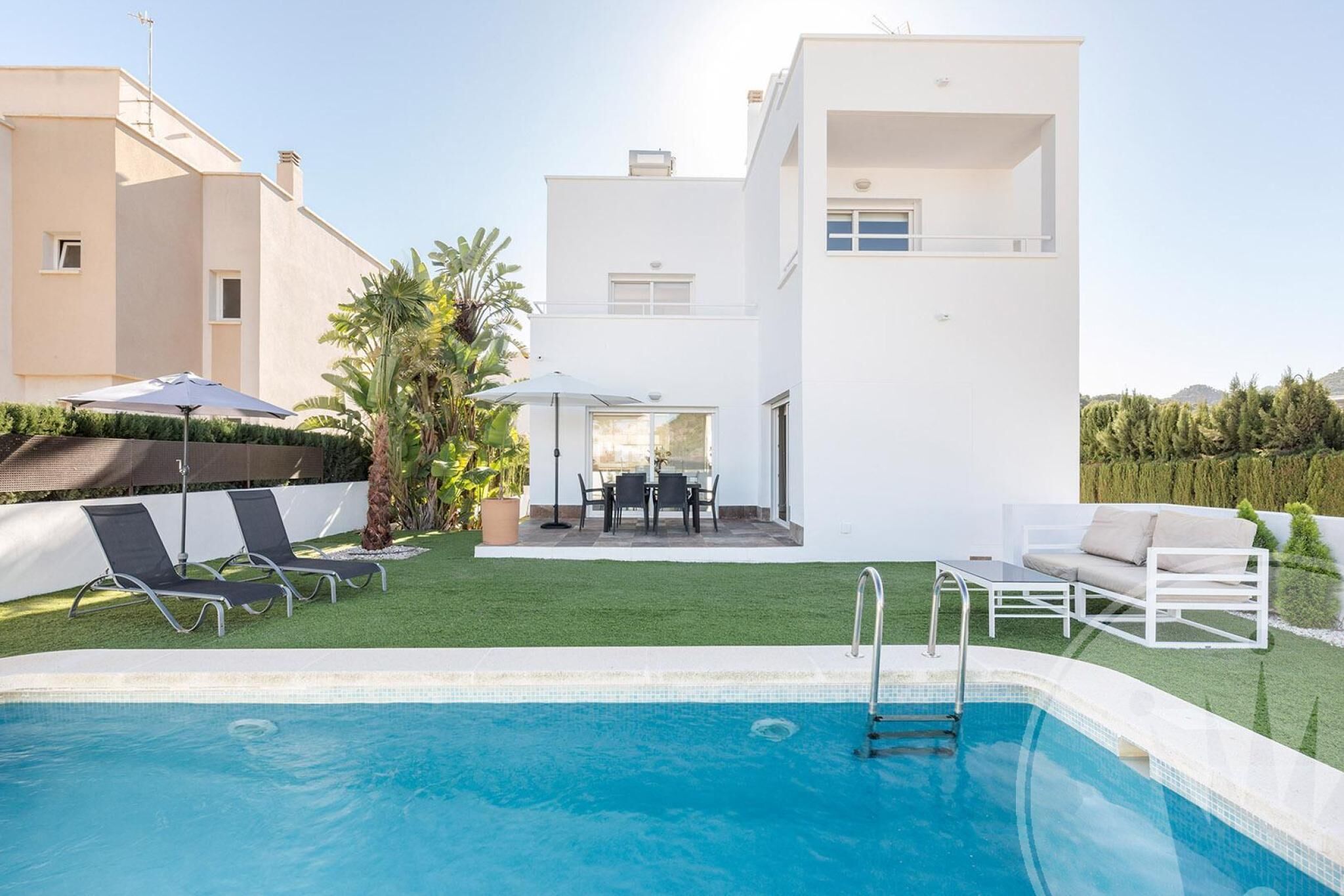 A modern house with a swimming pool, a patio with outdoor furniture, and a well-maintained lawn.