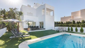 A modern two-story house with a swimming pool, outdoor seating, and a well-maintained lawn.