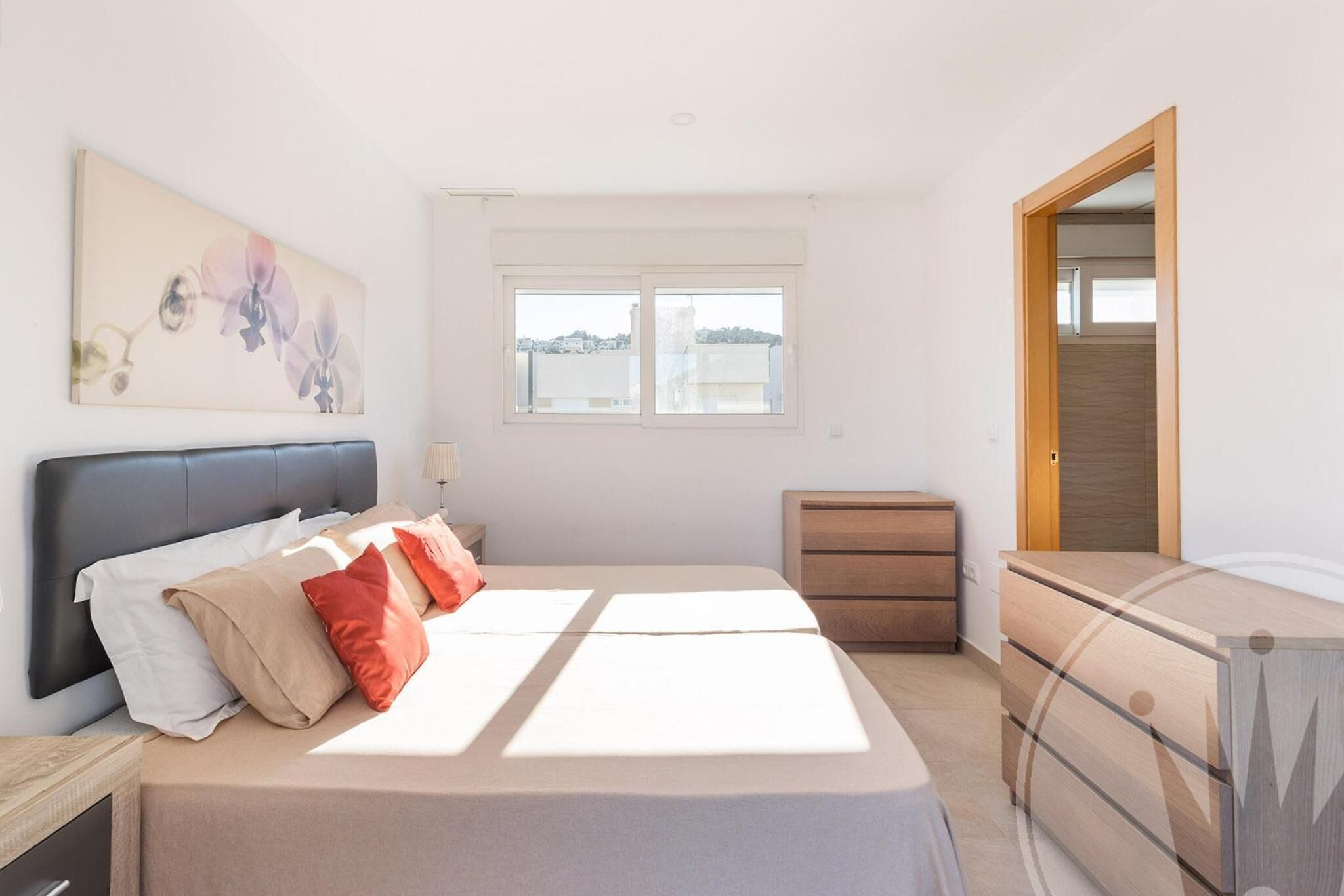 A bedroom with a bed, a dresser, a nightstand, a window with a view, and a painting on the wall.