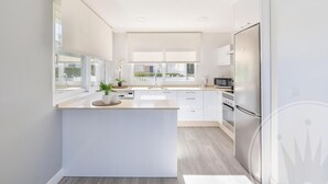 A modern kitchen with a central island, white cabinetry, stainless steel appliances, and large windows.