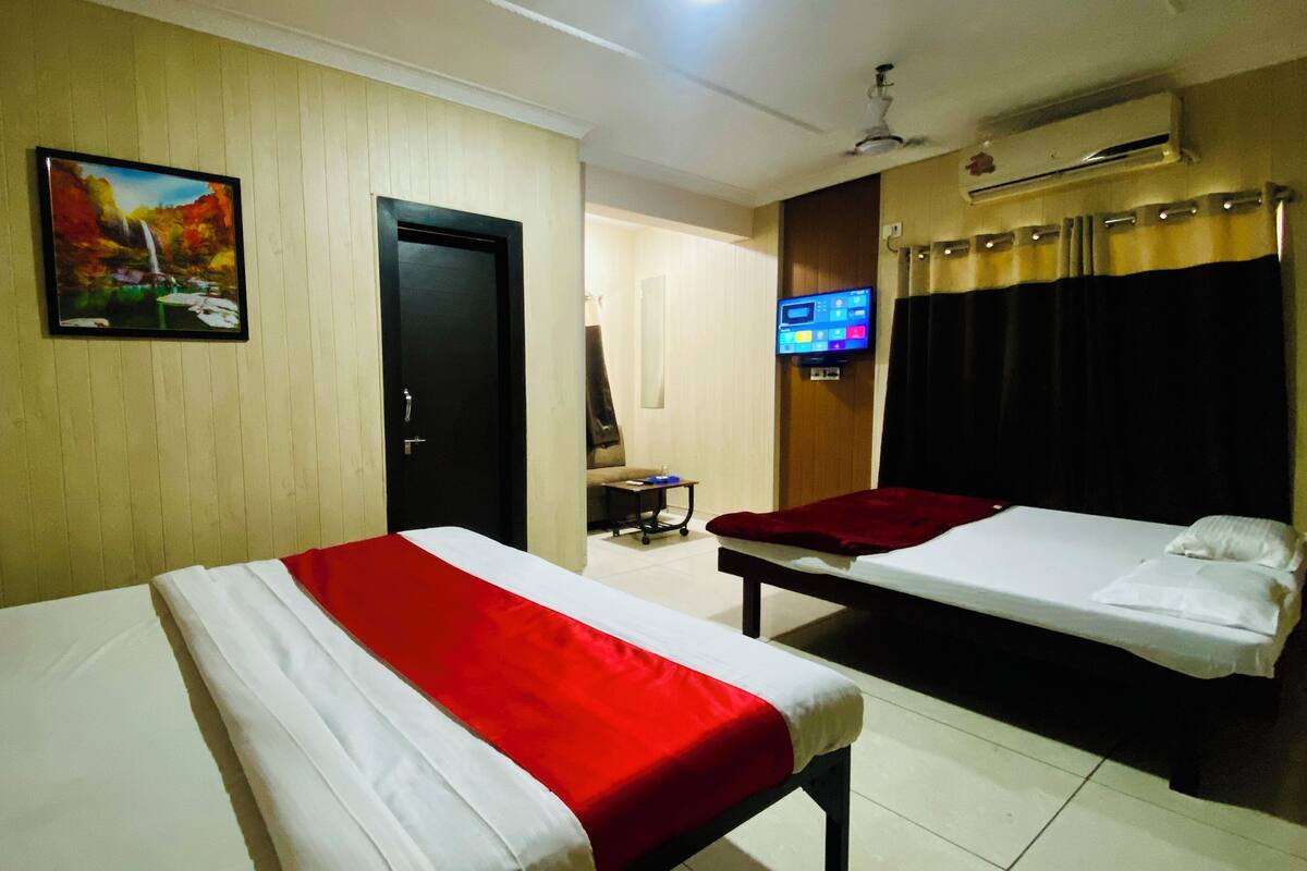 A hotel room with two beds, a TV, an air conditioner, and a painting on the wall.