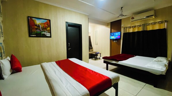 A hotel room with two beds, a TV, an air conditioner, and a painting on the wall.