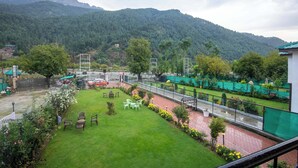 A view of a lush green lawn with a seating area and a paved walkway. - Hotel Riviera By Mount view (Anantnag)